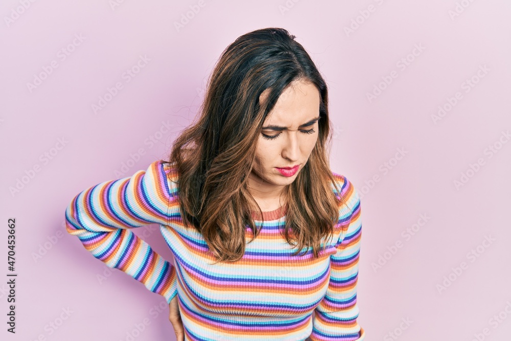 Young hispanic girl wearing casual clothes suffering of backache, touching back with hand, muscular pain Young hispanic girl wearing casual clothes suffering of backache, touching back with hand, muscular pain