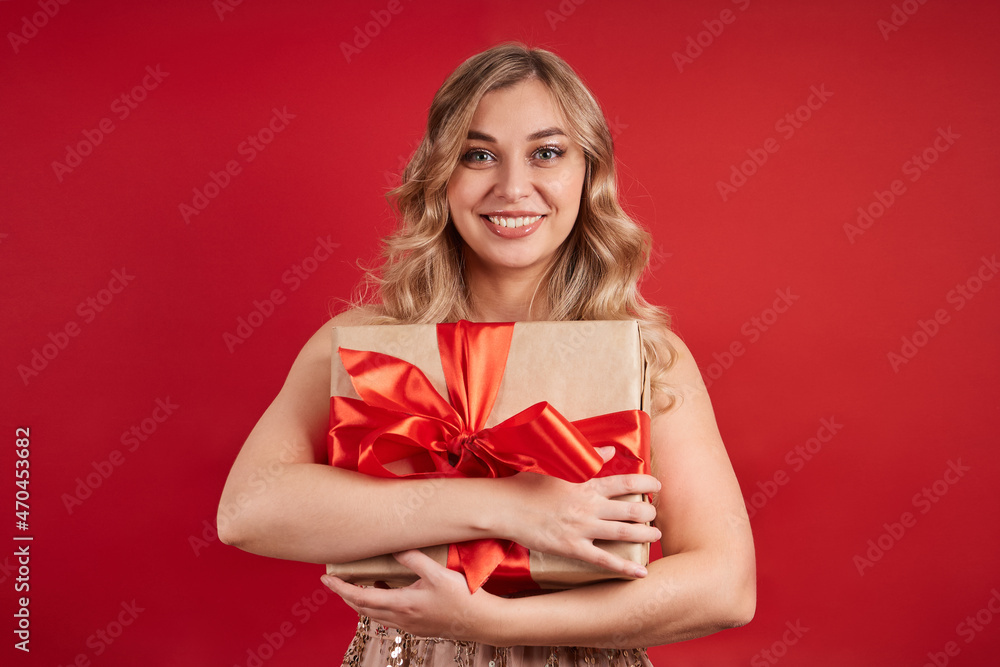 Emotional blonde is happy with the gift, looks at the camera. Isolate on a red background. Happy New Year, Merry Christmas, Happy Valentine's Day Emotional blonde is happy with the gift, looks at the camera. Isolate on a red background. Happy New Year, Merry Christmas, Happy Valentine's Day