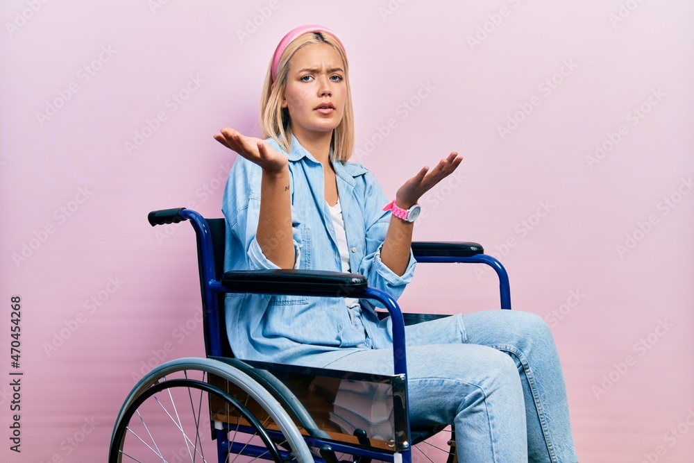 Beautiful blonde woman sitting on wheelchair clueless and confused with open arms, no idea concept. Beautiful blonde woman sitting on wheelchair clueless and confused with open arms, no idea concept.