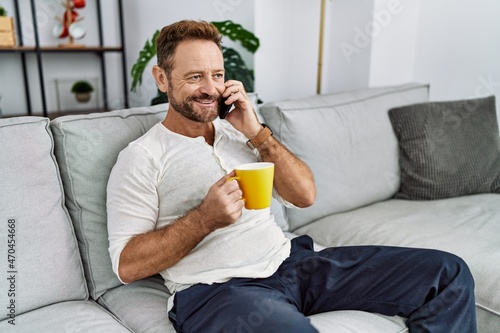 Middle age hispanic man talking on the smartphone drinking coffee at home