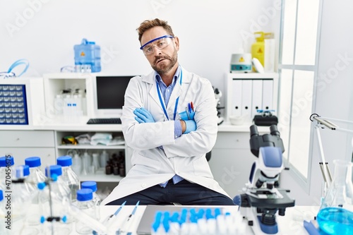 Middle age man working at scientist laboratory skeptic and nervous, disapproving expression on face with crossed arms. negative person.
