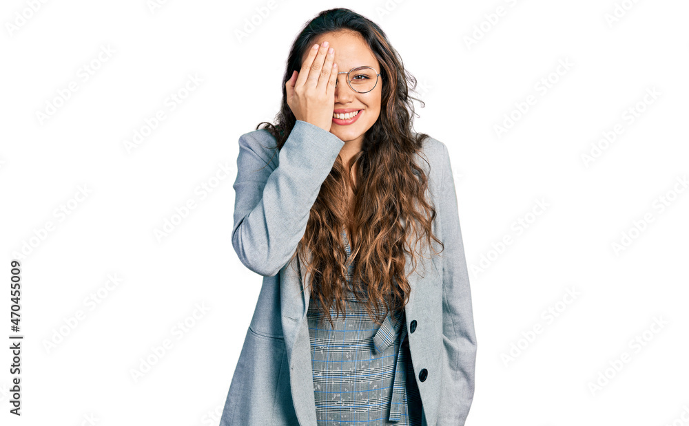 Young hispanic girl wearing business clothes and glasses covering one eye with hand, confident smile on face and surprise emotion. Young hispanic girl wearing business clothes and glasses covering one eye with hand, confident smile on face and surprise emotion.