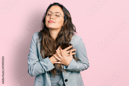 Young hispanic girl wearing business clothes and glasses smiling with hands on chest with closed eyes and grateful gesture on face. health concept.