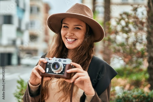 Young hispanic tourist woman smiling happy using vintage camera at the city.