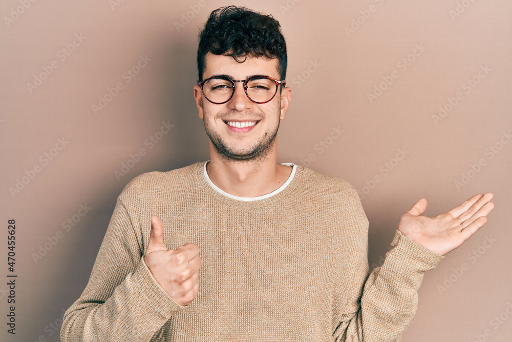 Young hispanic man wearing casual clothes and glasses showing palm hand and doing ok gesture with thumbs up, smiling happy and cheerful Young hispanic man wearing casual clothes and glasses showing palm hand and doing ok gesture with thumbs up, smiling happy and cheerful