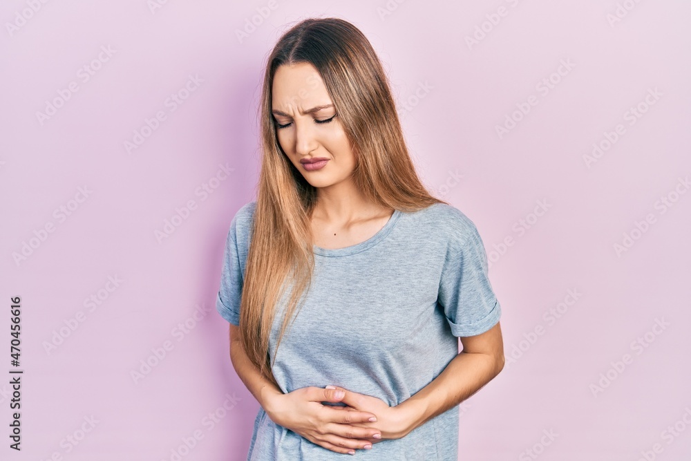 Young blonde girl wearing casual t shirt with hand on stomach because indigestion, painful illness feeling unwell. ache concept.