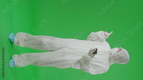 Full Body Of Asian Man Wearing Personal Protective Equipment Uniform Ppe, Medical Face Mask And Use Mobile Phone With Pointing To The Side In The Green Screen Studio
 photo