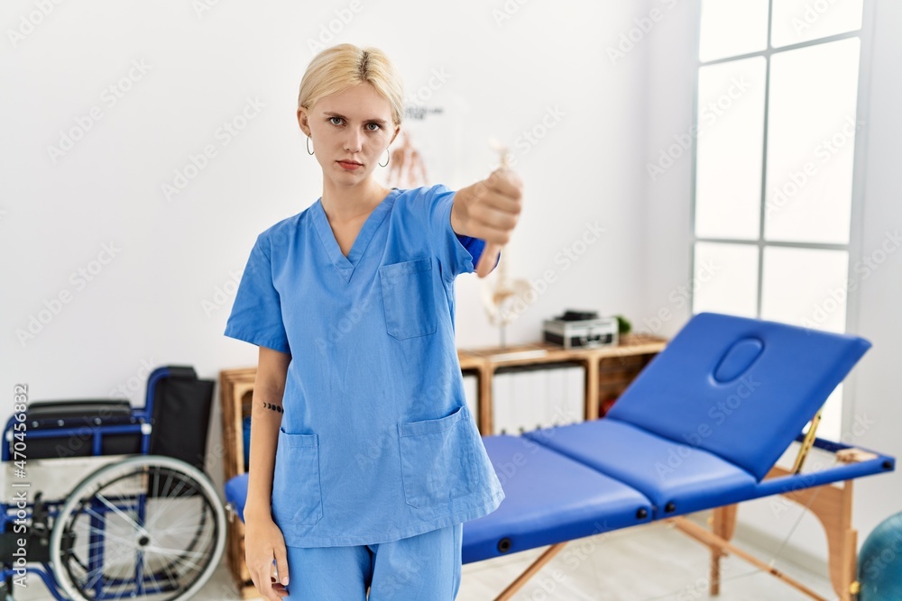 Beautiful caucasian physiotherapist woman working at pain recovery clinic looking unhappy and angry showing rejection and negative with thumbs down gesture. bad expression. Beautiful caucasian physiotherapist woman working at pain recovery clinic looking unhappy and angry showing rejection and negative with thumbs down gesture. bad expression.