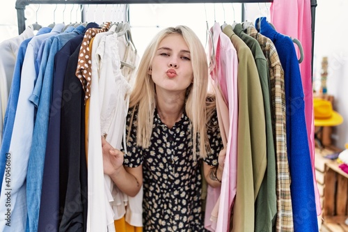Young blonde woman searching clothes on clothing rack looking at the camera blowing a kiss being lovely and sexy. love expression.