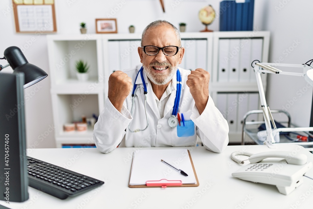 Obraz premium Mature doctor man at the clinic excited for success with arms raised and eyes closed celebrating victory smiling. winner concept.