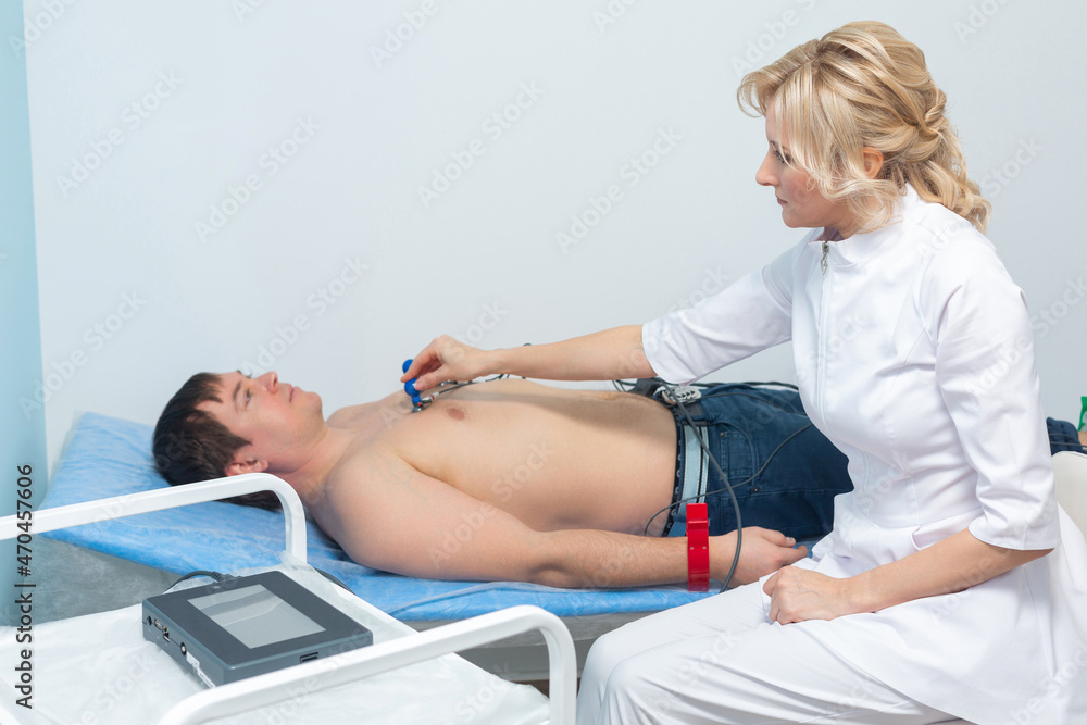 Obraz premium A cardiologist doctor applies sensors to the naked body of a man lying on a couch during an electrocardiography procedure in a hospital