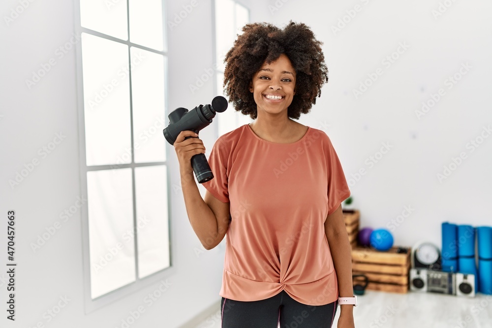 Young african american woman smiling confident holding percussion pistol at sport center Young african american woman smiling confident holding percussion pistol at sport center