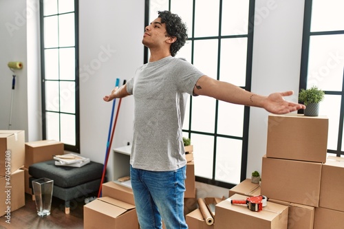 Young hispanic man breathing with open arms standing at new home.