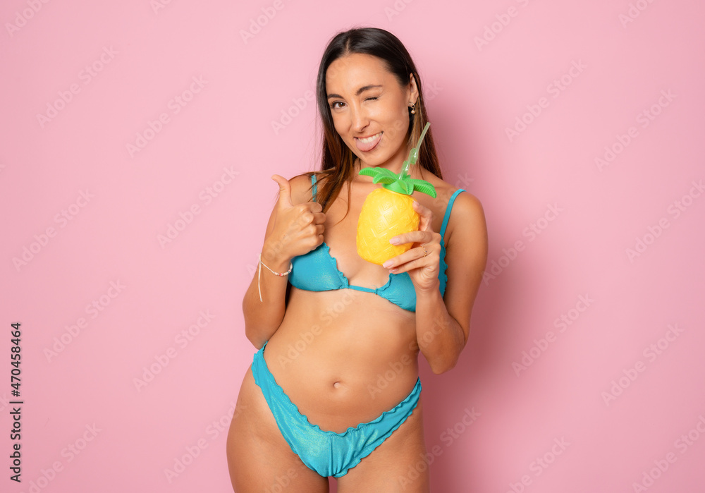 Naklejka premium Beautiful smiling woman in bikini drinking juice isolated over pink background.