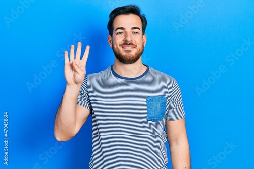 Handsome caucasian man with beard wearing casual striped t shirt showing and pointing up with fingers number four while smiling confident and happy. © Krakenimages.com
