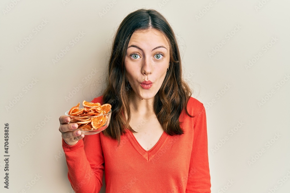 Young brunette woman holding bowl of dry orange scared and amazed with open mouth for surprise, disbelief face Young brunette woman holding bowl of dry orange scared and amazed with open mouth for surprise, disbelief face