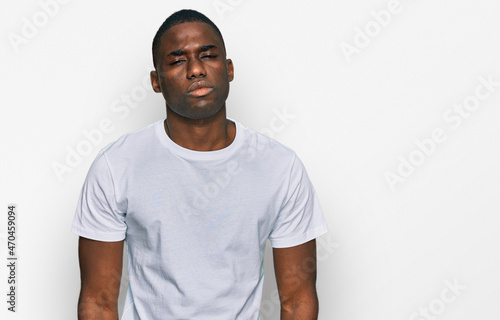 Young african american man wearing casual white t shirt looking sleepy and tired, exhausted for fatigue and hangover, lazy eyes in the morning.
