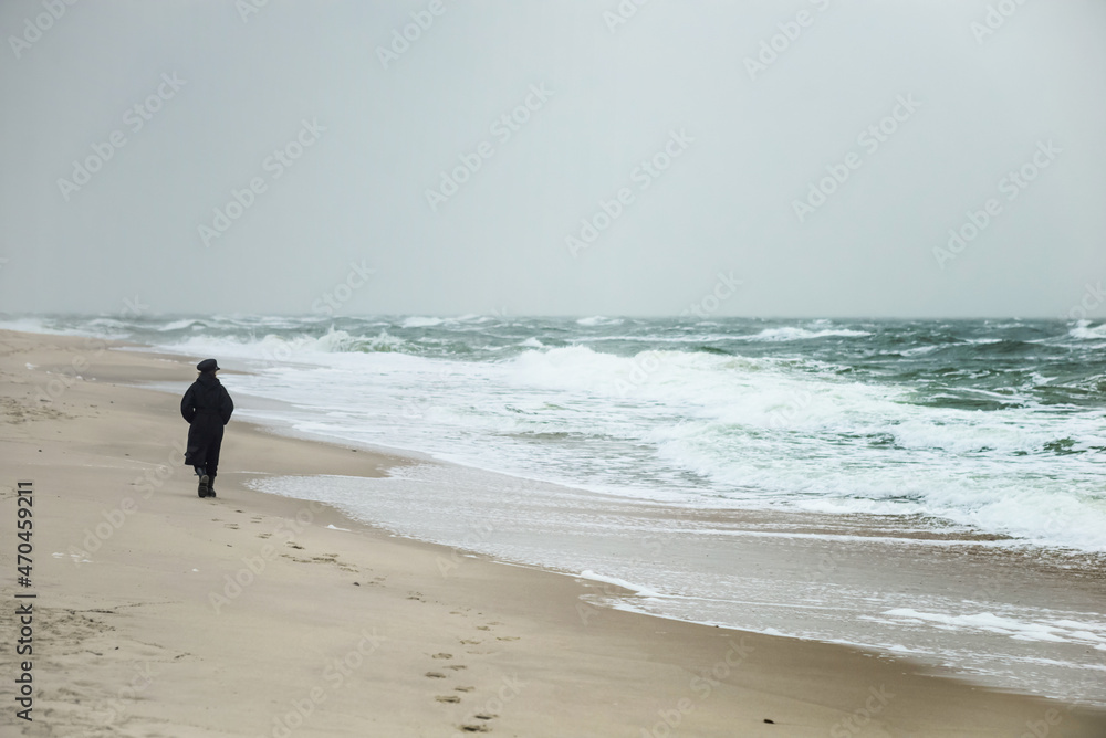 a lonely girl in a black long coat on the coast of a stormy sea in a storm