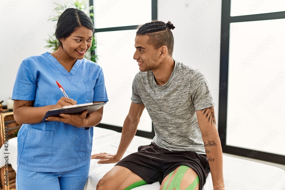 Fototapeta premium Young latin physioterapist woman asking to patient at the clinic.