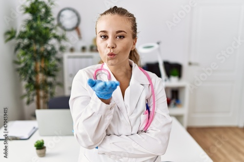 Young caucasian woman wearing doctor uniform and stethoscope at the clinic looking at the camera blowing a kiss with hand on air being lovely and sexy. love expression.