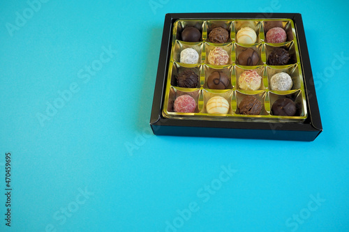 many different round chocolate truffles lie in a box on a blue background. side view.  high-calorie sweets. copy space © NataSel