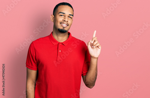 Young african american man wearing casual polo smiling with an idea or question pointing finger up with happy face, number one