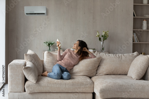Photos Smiling woman using air conditioner remote controller, relaxing on comfortable c