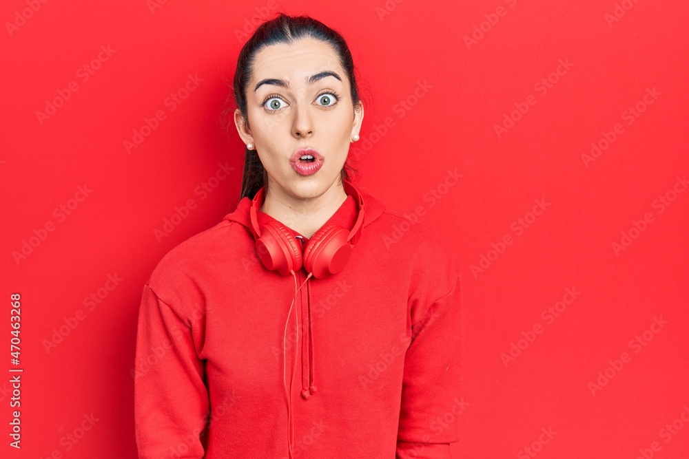 Beautiful woman with blue eyes wearing gym clothes and headphones scared and amazed with open mouth for surprise, disbelief face Beautiful woman with blue eyes wearing gym clothes and headphones scared and amazed with open mouth for surprise, disbelief face