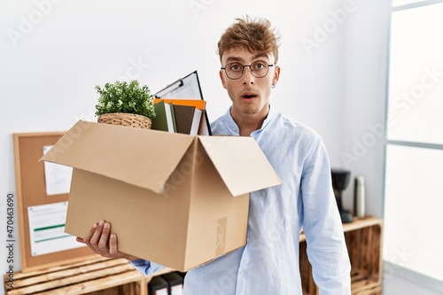 Young caucasian man holding business box scared and amazed with open mouth for surprise, disbelief face