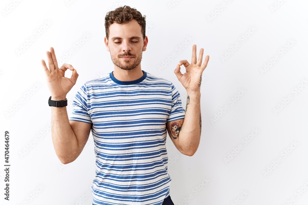 Handsome young man standing over isolated background relaxed and smiling with eyes closed doing meditation gesture with fingers. yoga concept. Handsome young man standing over isolated background relaxed and smiling with eyes closed doing meditation gesture with fingers. yoga concept.