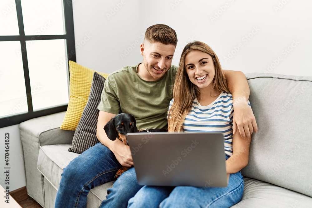 Young hispanic couple smiling happy using laptop sitting on the sofa  with dog at home.
