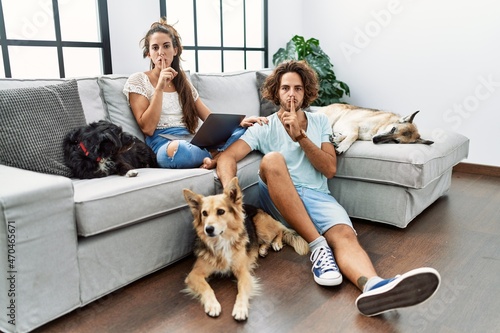 Canvas Print Young hispanic couple with dogs relaxing at home asking to be quiet with finger on lips