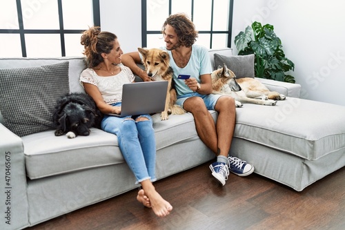 Photography Man and woman couple using laptop and credit card sitting on sofa with dogs at h
