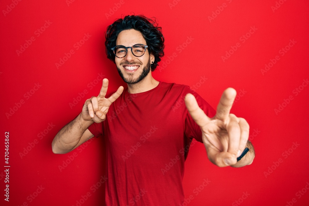 Naklejka premium Handsome hispanic man wearing casual t shirt and glasses smiling looking to the camera showing fingers doing victory sign. number two.