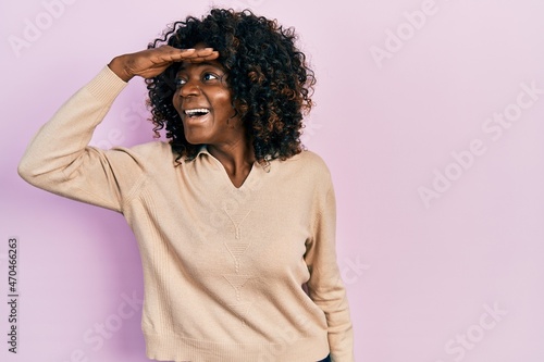 Young african american woman wearing casual clothes very happy and smiling looking far away with hand over head. searching concept.