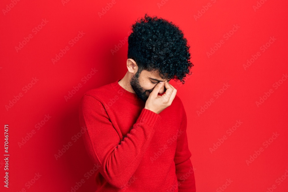 Young arab man with beard wearing casual red sweater tired rubbing nose and eyes feeling fatigue and headache. stress and frustration concept. Young arab man with beard wearing casual red sweater tired rubbing nose and eyes feeling fatigue and headache. stress and frustration concept.