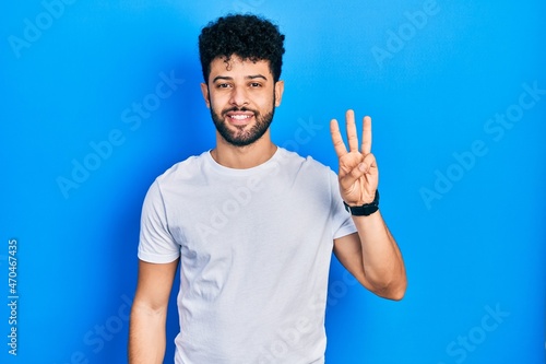 Young arab man with beard wearing casual white t shirt showing and pointing up with fingers number three while smiling confident and happy. © Krakenimages.com