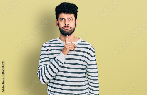 Young arab man with beard wearing casual striped sweater thinking concentrated about doubt with finger on chin and looking up wondering