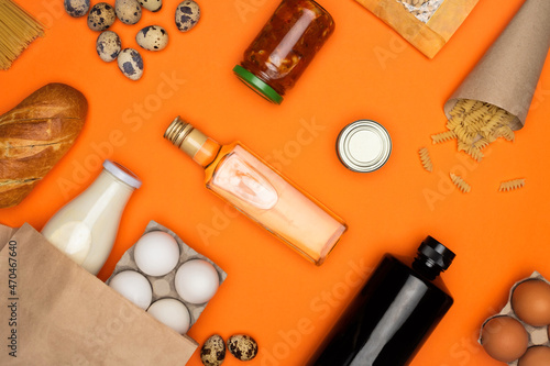 Eggs and bottle of milk in paper eco bag. Spaghetti, bread, quail eggs, beans, tomato paste on orange background