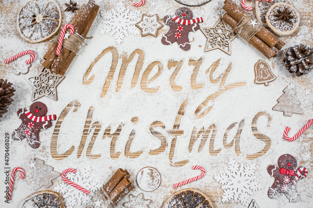 The inscription on the flour Merry Christmas. A frame of gingerbread men, cinnamon, cookies, lollipops and Christmas decorations on a wooden background. The concept of cafes and restaurants. The inscription on the flour Merry Christmas. A frame of gingerbread men, cinnamon, cookies, lollipops and Christmas decorations on a wooden background. The concept of cafes and restaurants.