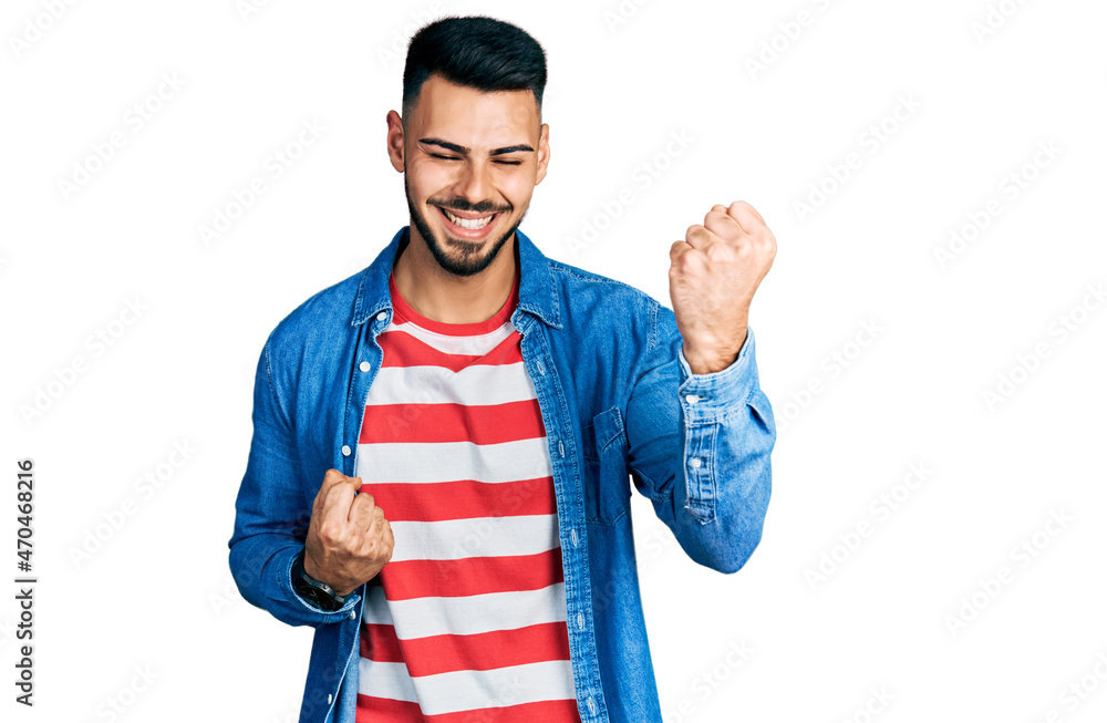 Young hispanic man with beard wearing casual denim jacket celebrating surprised and amazed for success with arms raised and eyes closed. winner concept. Young hispanic man with beard wearing casual denim jacket celebrating surprised and amazed for success with arms raised and eyes closed. winner concept.
