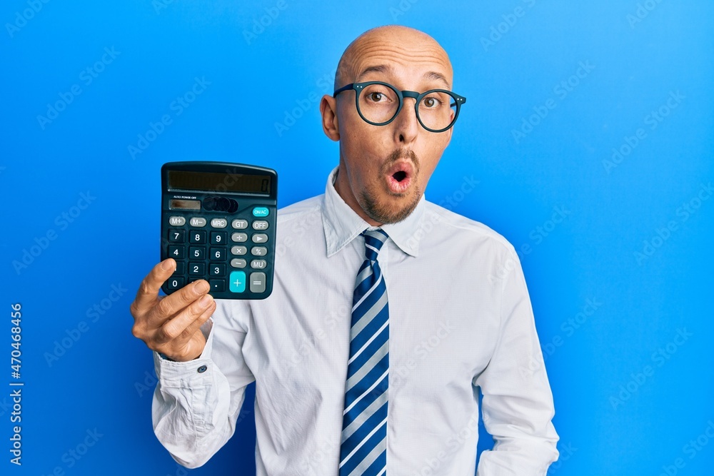 Bald business man with beard showing calculator device scared and amazed with open mouth for surprise, disbelief face Bald business man with beard showing calculator device scared and amazed with open mouth for surprise, disbelief face