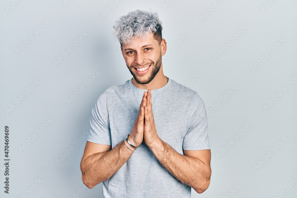 Young hispanic man with modern dyed hair wearing casual grey t shirt praying with hands together asking for forgiveness smiling confident. Young hispanic man with modern dyed hair wearing casual grey t shirt praying with hands together asking for forgiveness smiling confident.