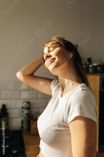 Attractive girl in a white T-shirt enjoys the sun in the kitchen