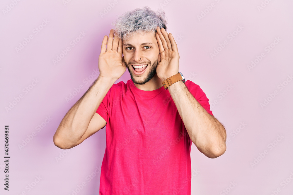Young hispanic man with modern dyed hair wearing casual pink t shirt smiling cheerful playing peek a boo with hands showing face. surprised and exited Young hispanic man with modern dyed hair wearing casual pink t shirt smiling cheerful playing peek a boo with hands showing face. surprised and exited