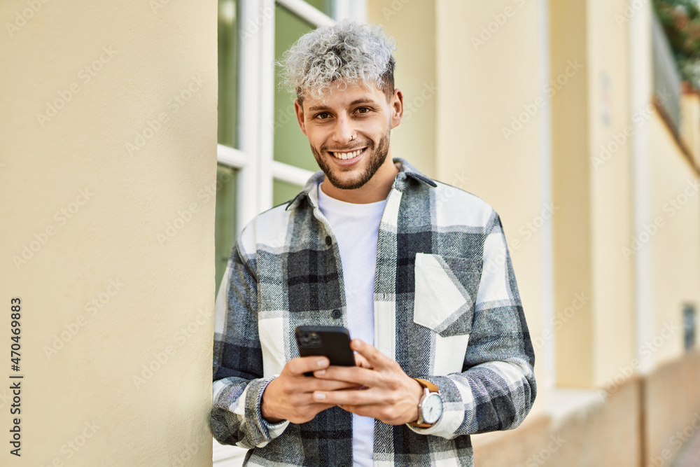 Fototapeta premium Young hispanic man smiling happy using smartphone at the city.