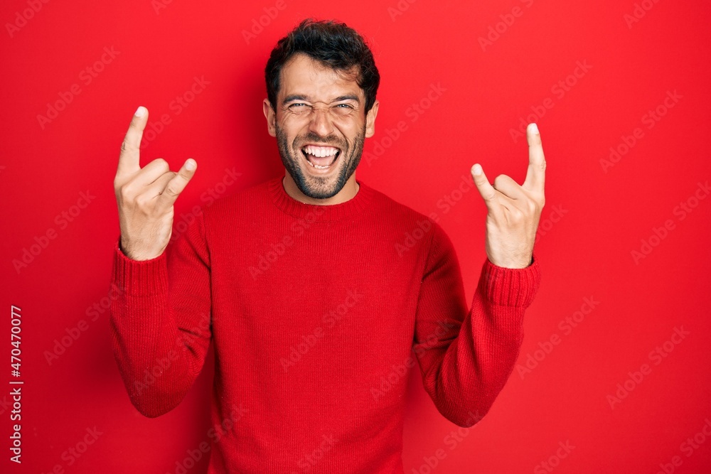 Handsome man with beard wearing casual red sweater shouting with crazy expression doing rock symbol with hands up. music star. heavy music concept. Handsome man with beard wearing casual red sweater shouting with crazy expression doing rock symbol with hands up. music star. heavy music concept.
