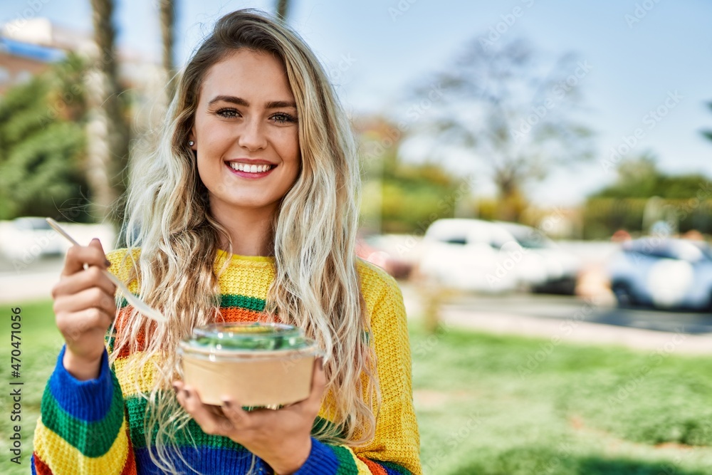 Fototapeta premium Young blonde woman eating healthy salad at the park