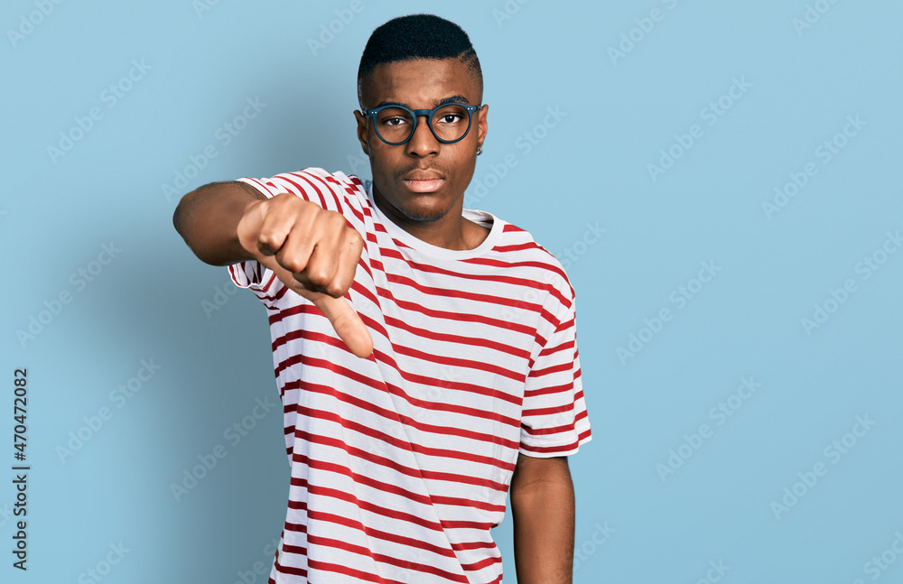Young african american man wearing casual t shirt and glasses looking unhappy and angry showing rejection and negative with thumbs down gesture. bad expression. Young african american man wearing casual t shirt and glasses looking unhappy and angry showing rejection and negative with thumbs down gesture. bad expression.
