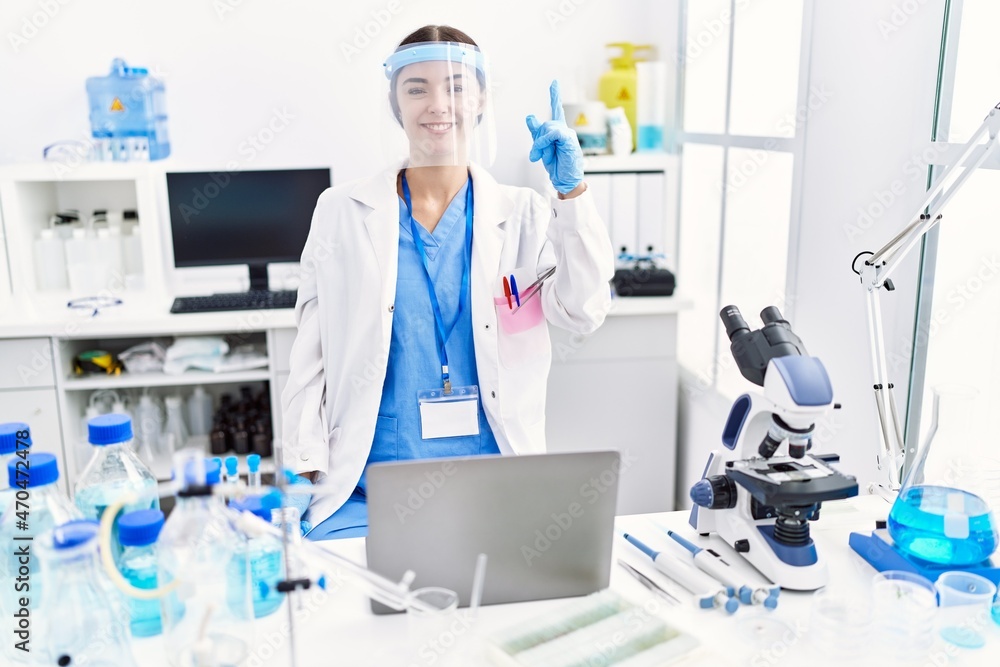 Young hispanic woman wearing scientist uniform pointing finger up with successful idea. exited and happy. number one. Young hispanic woman wearing scientist uniform pointing finger up with successful idea. exited and happy. number one.